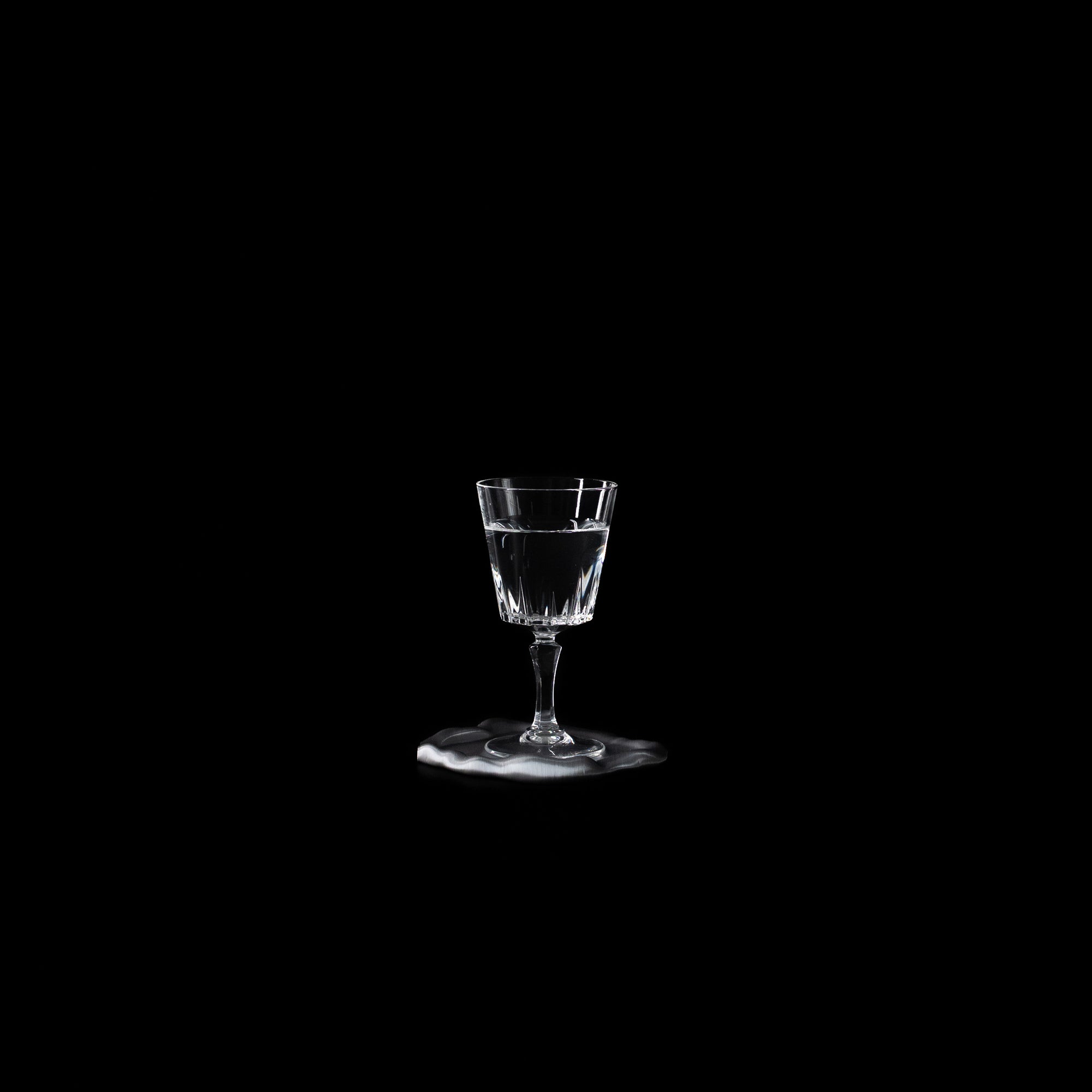 Dessous de verre Fuso en PLA chromé avec un verre à pied, photographié sur fond noir