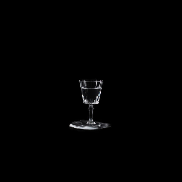 Dessous de verre Fuso en PLA chromé avec un verre à pied, photographié sur fond noir