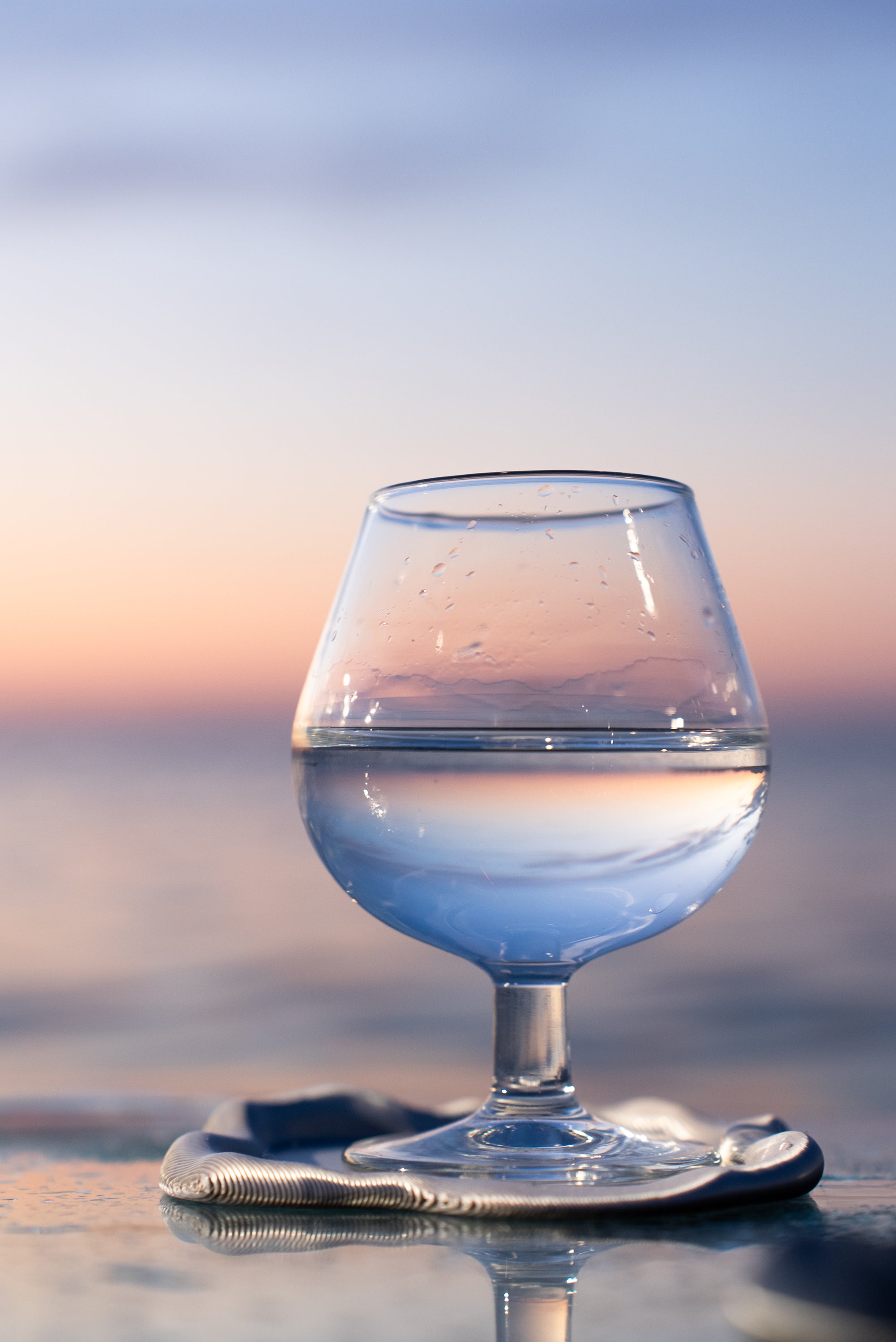 Zoom sur le dessous de verre FUSO de S7DE Studio avec un verre posé dessus, au lever du soleil sur une table en verre.