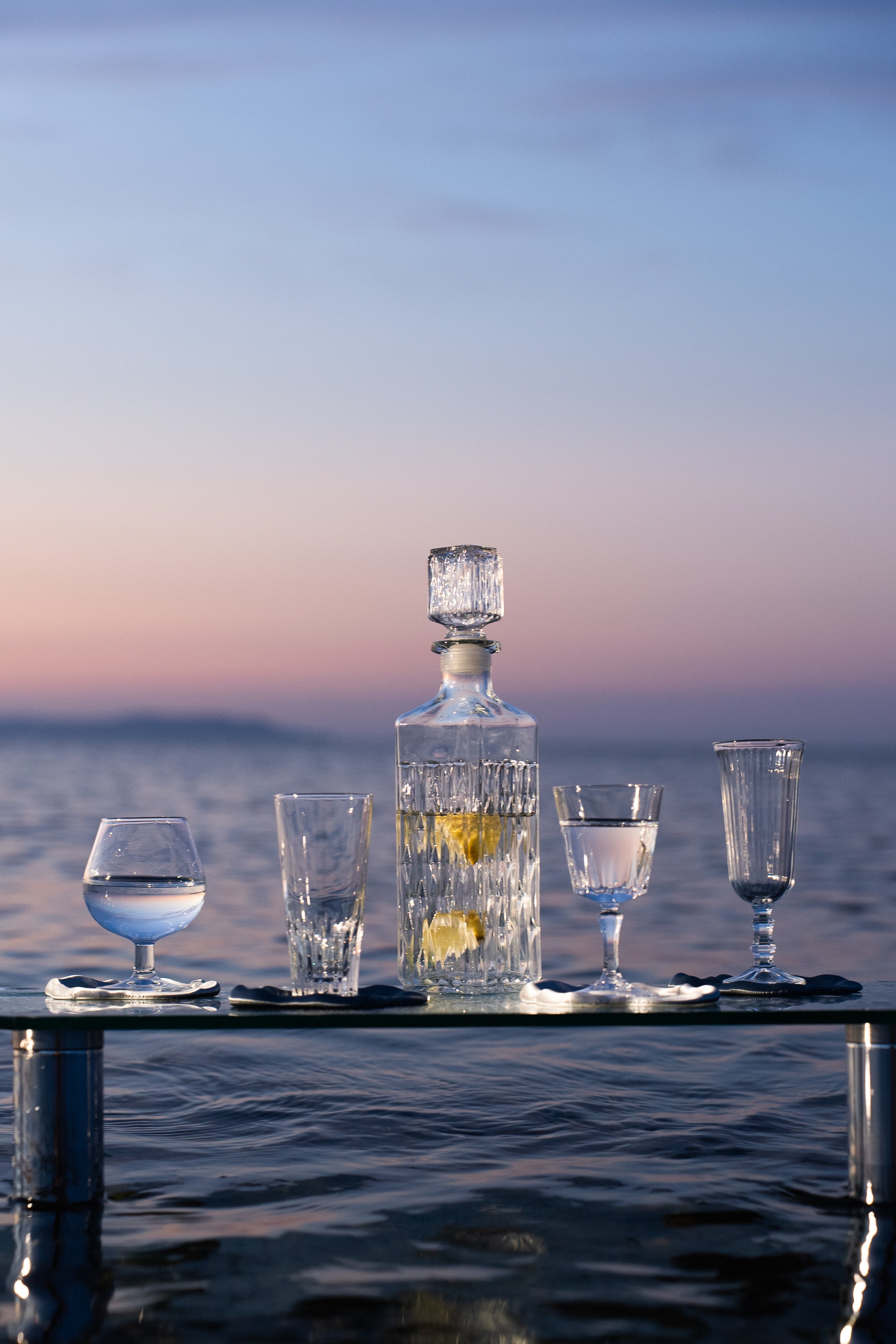 Dessous de verre FUSO de S7DE Studio posé sur une table en verre dans la mer au lever du soleil.