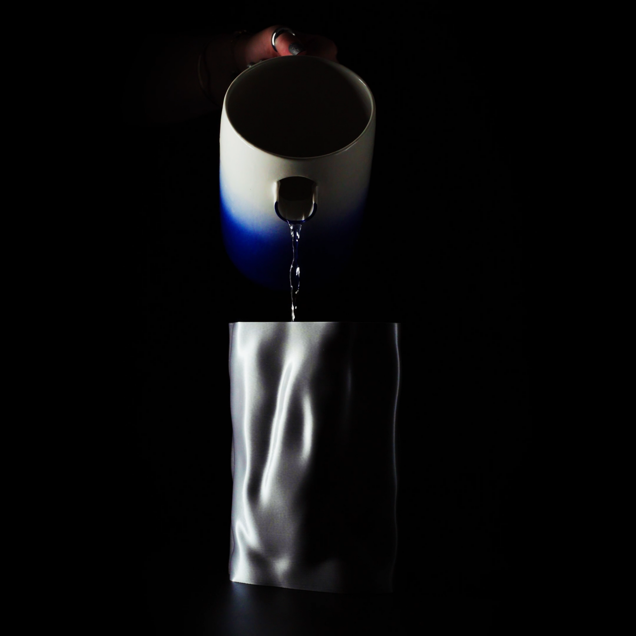 Vase Aura sur fond noir avec son insert en train d'être rempli par un pichet