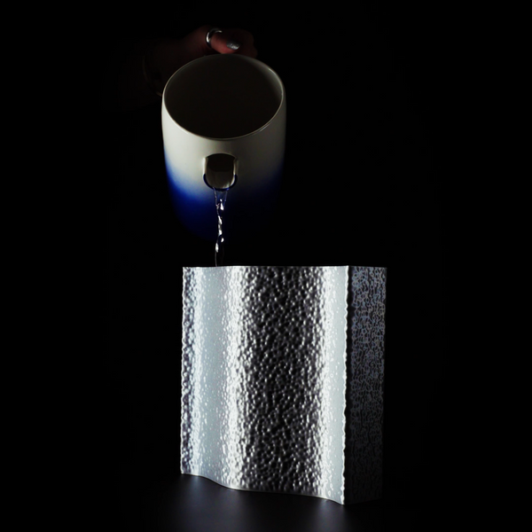 Vase Mira sur fond noir avec son insert en train d'être rempli par un pichet