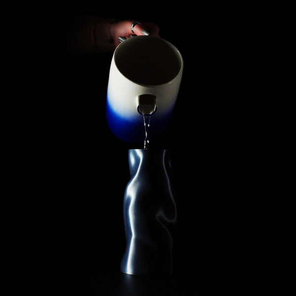 Vase Riflesso sur fond noir avec son insert en train d'être rempli par un pichet