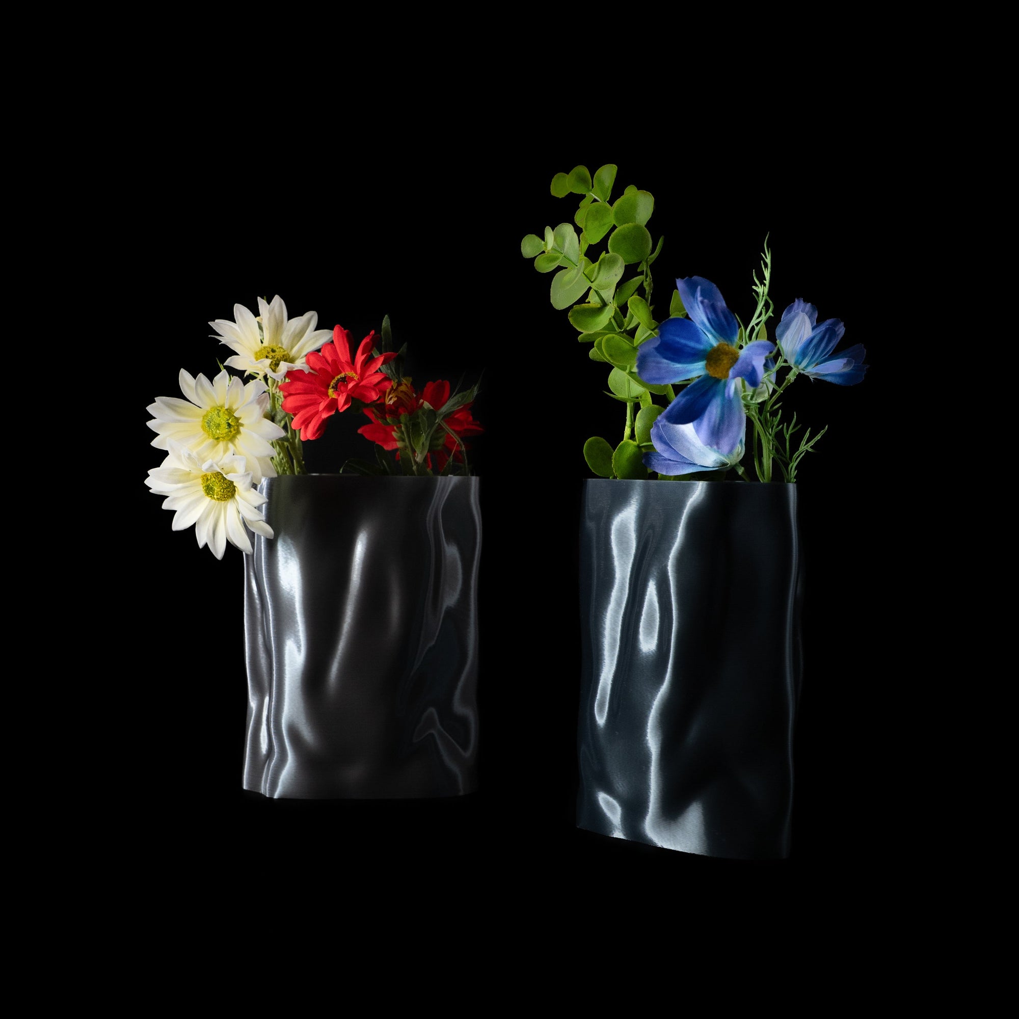 Deux vases Aura en PLA chromé, garnis de fleurs blanches, rouges et bleues, photographiés sur fond noir