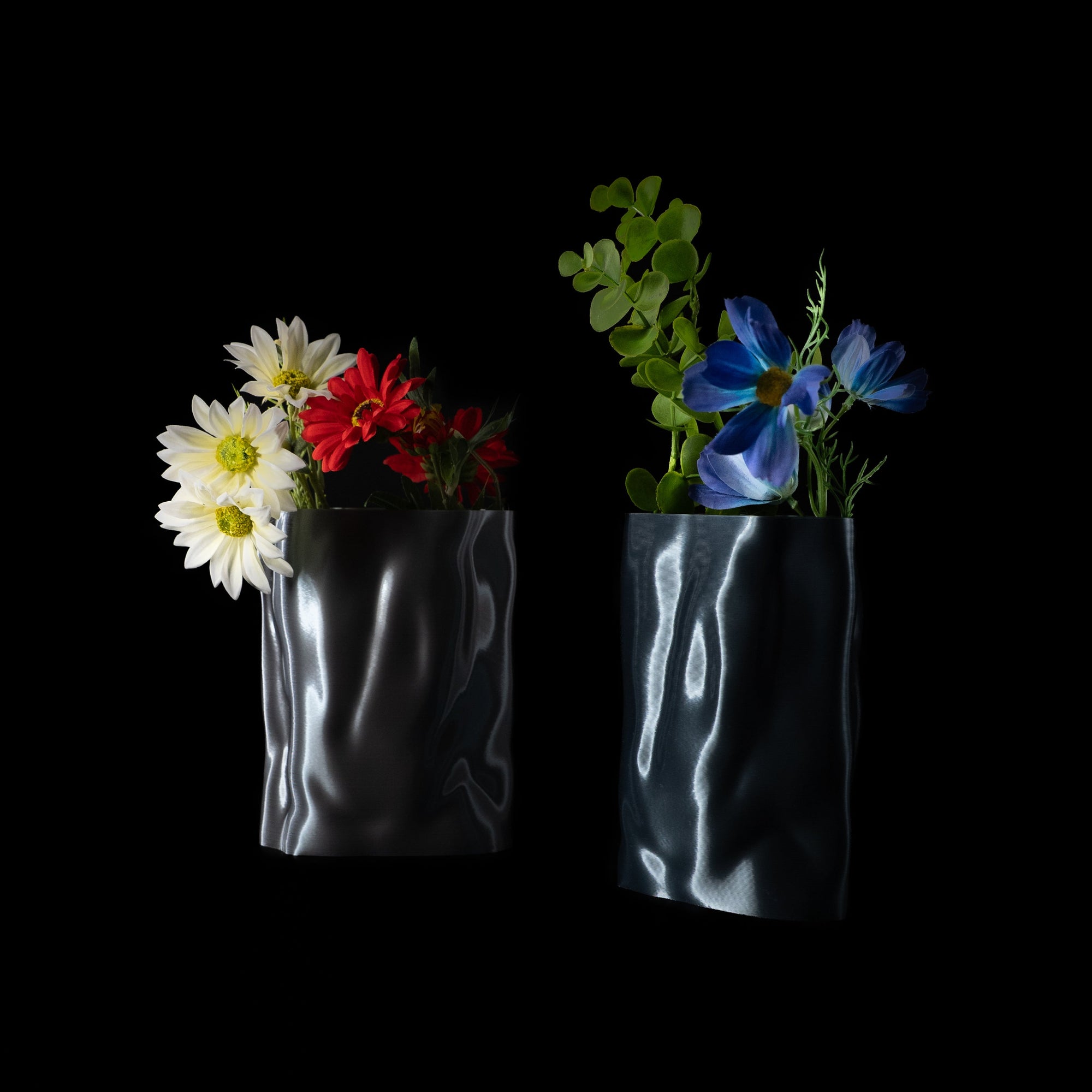 Deux vases Aura en PLA chromé, garnis de fleurs blanches, rouges et bleues, photographiés sur fond noir