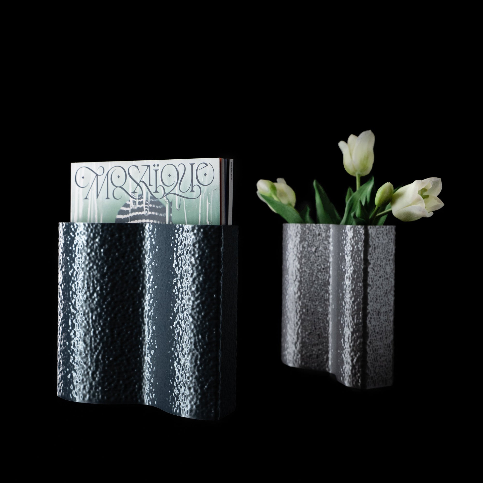 Deux vases Mira en PLA chromé, l’un avec des tulipes blanches, l’autre utilisé comme porte-magazine, sur fond noir