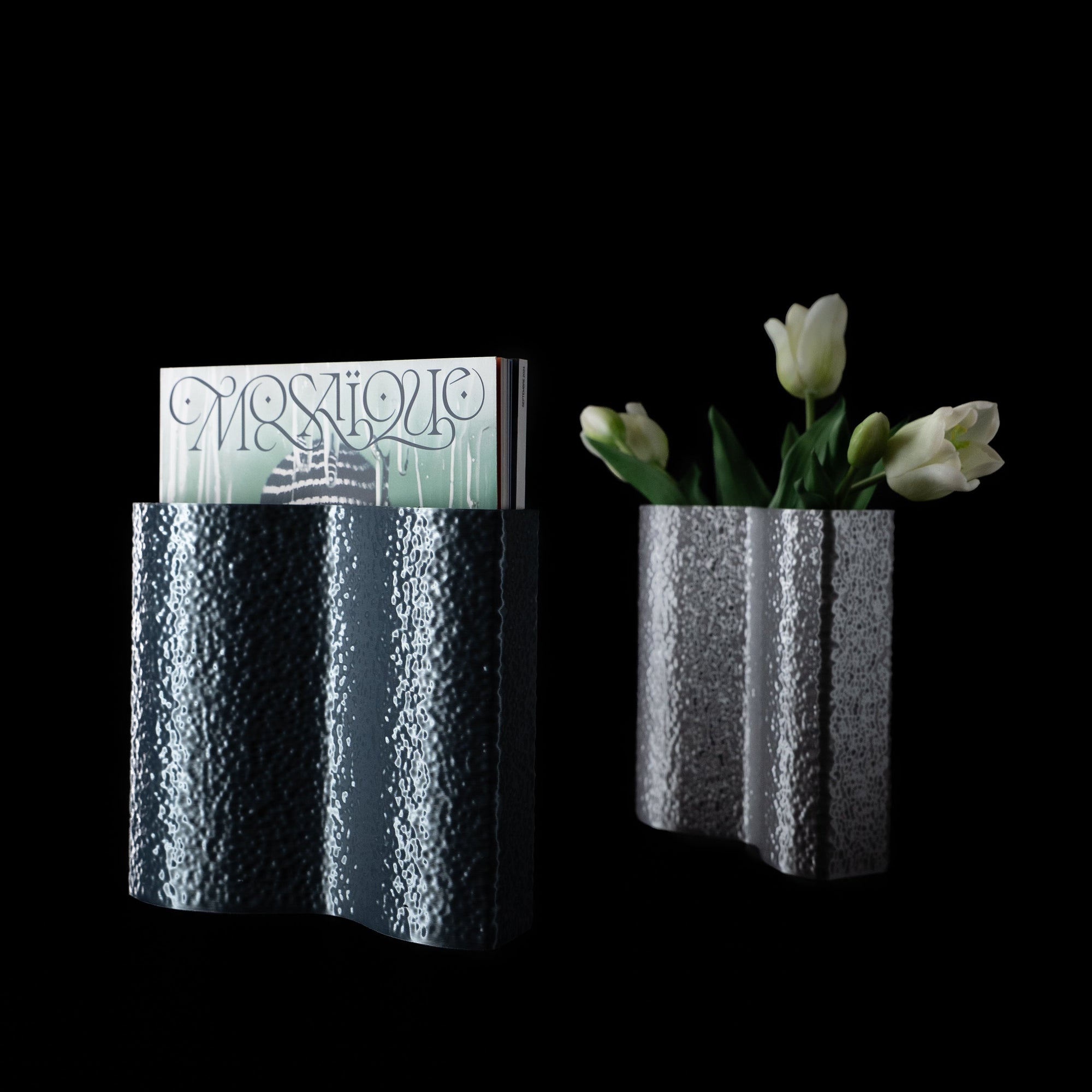 Deux vases Mira en PLA chromé, l’un avec des tulipes blanches, l’autre utilisé comme porte-magazine, sur fond noir
