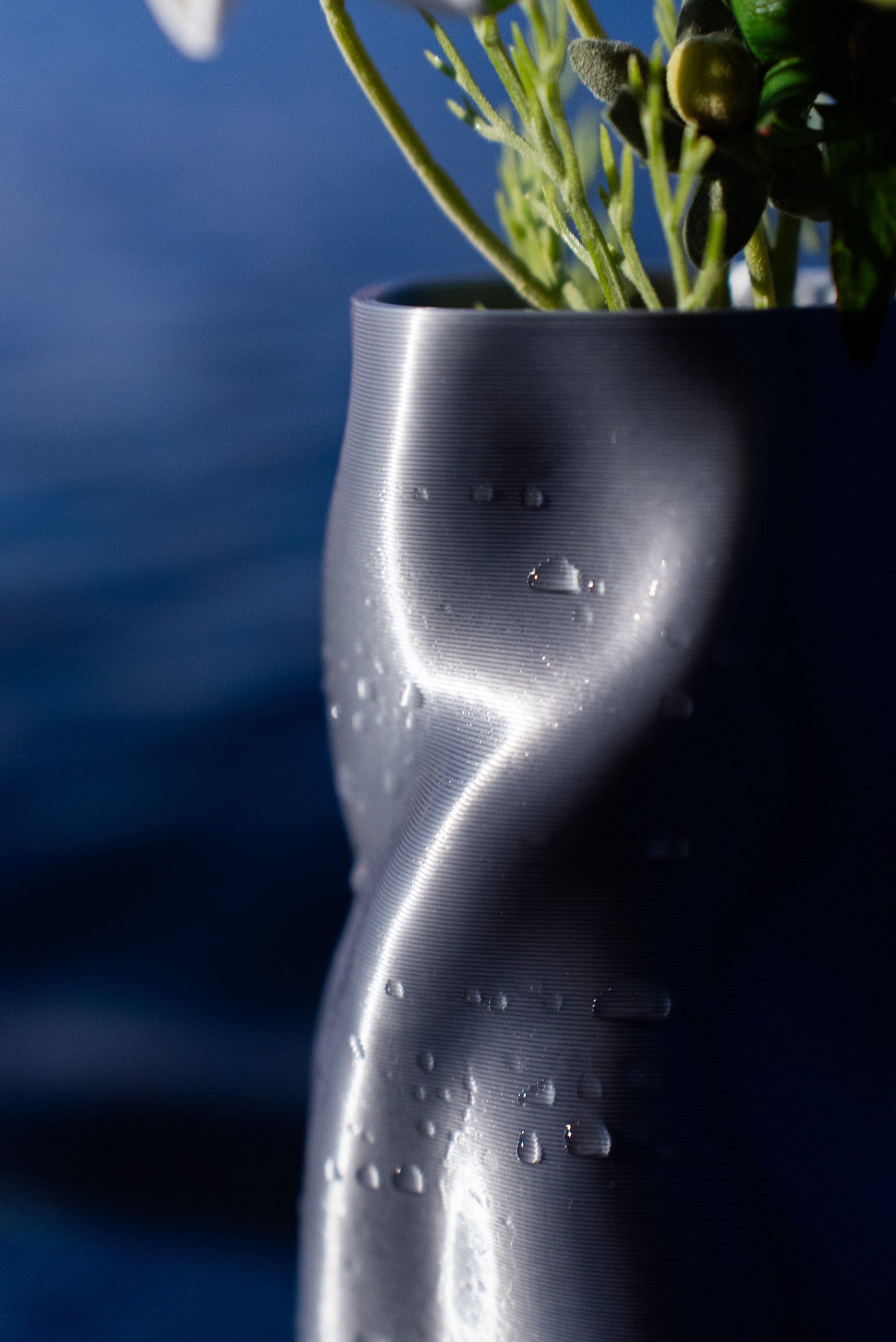 Vase Riflesso en PLA chromé de la collection Chrome Core, garni de fleurs, posé au bord de la mer au coucher du soleil vu de près