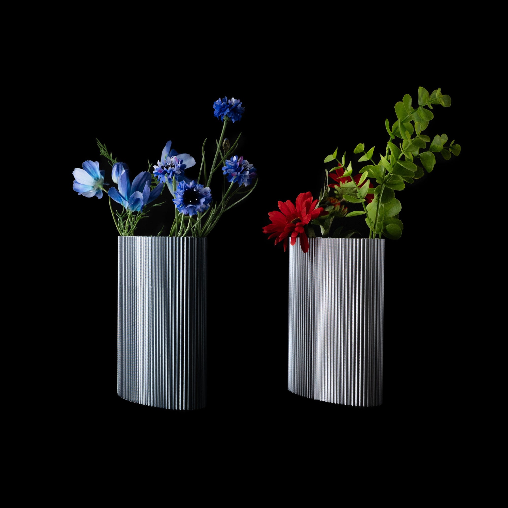 Deux vases Riga en PLA chromé, garnis de fleurs bleues et rouges, photographiés sur fond noir