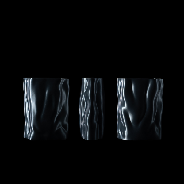 Trois vases Aura en coloris Aether présentés de face et partiellement pivotés pour révéler différentes facettes du design fluide et métallique, sur fond noir.