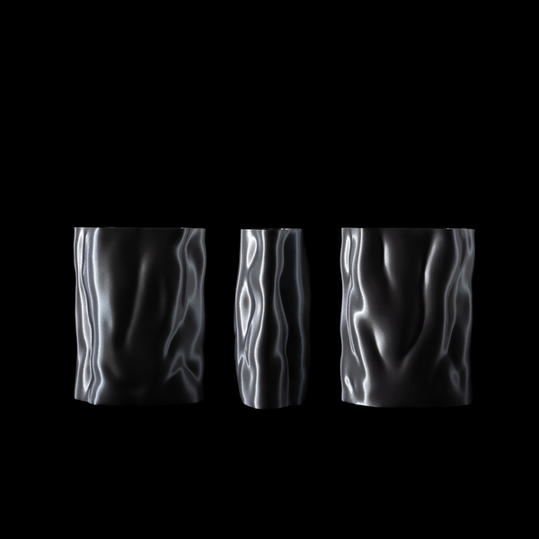 Trio de vases Aura en coloris Chrome tournés légèrement pour dévoiler la texture ondulée et les reflets lumineux sur fond noir.