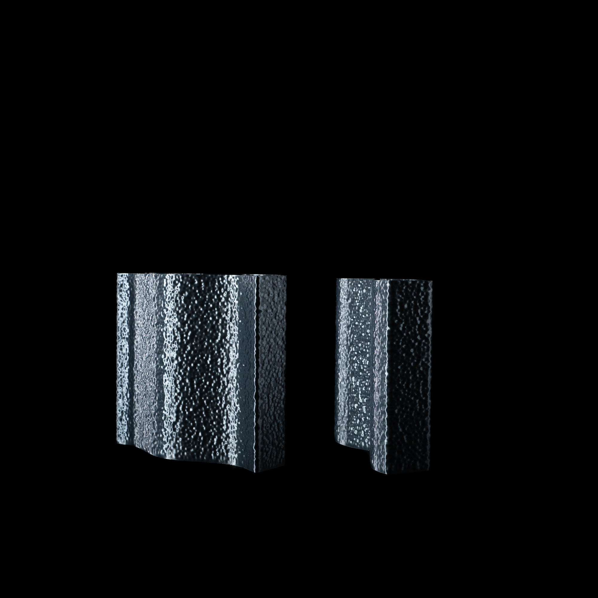 Deux vases Mira en PLA finition Aether, au design sculptural et texturé, présentés sur fond noir. Leur surface évoque une matière minérale aux reflets subtils.