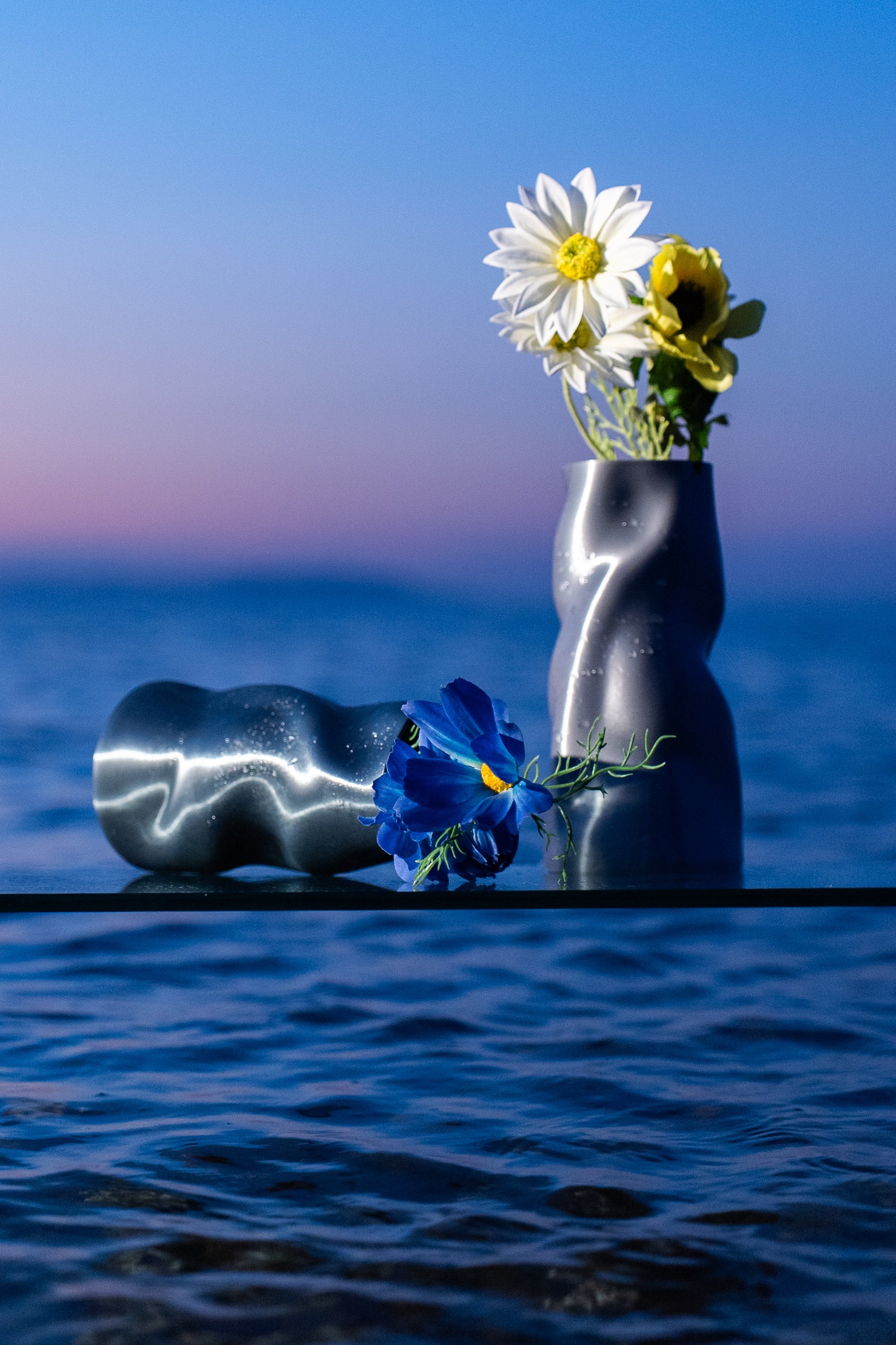 Duo de vases Riflesso en Chrome et Aether posés sur une table au lever du soleil.