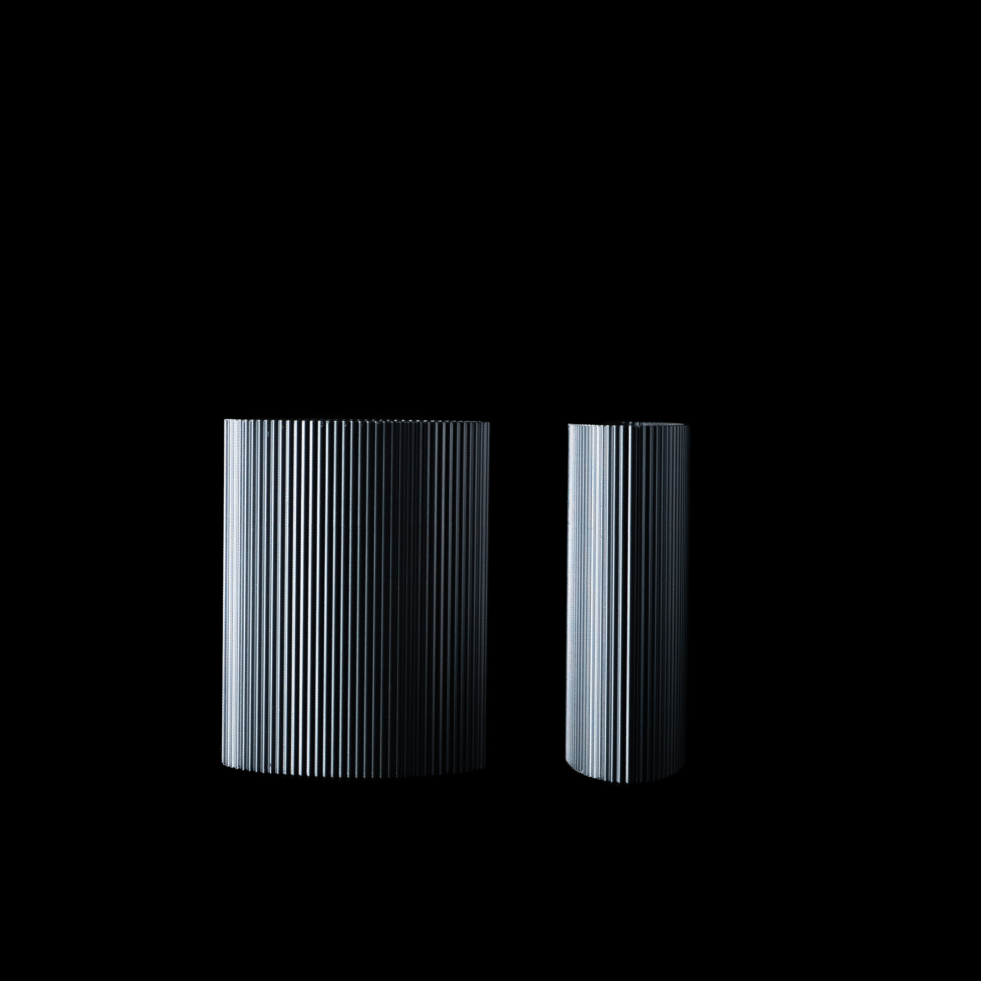 Deux vases Riga en PLA finition Aether, sur fond noir. Présentation en vue alternative pour révéler les stries verticales sous un autre angle de lumière.