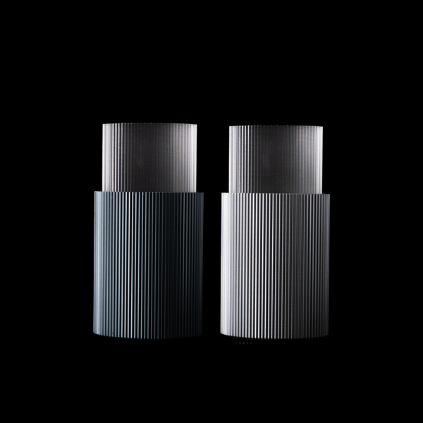 Deux vases Riga sur fond noir, l’un en finition Aether à gauche et l’autre en Chrome à droite. Les deux modèles sont équipés d’un insert transparent en PETG.