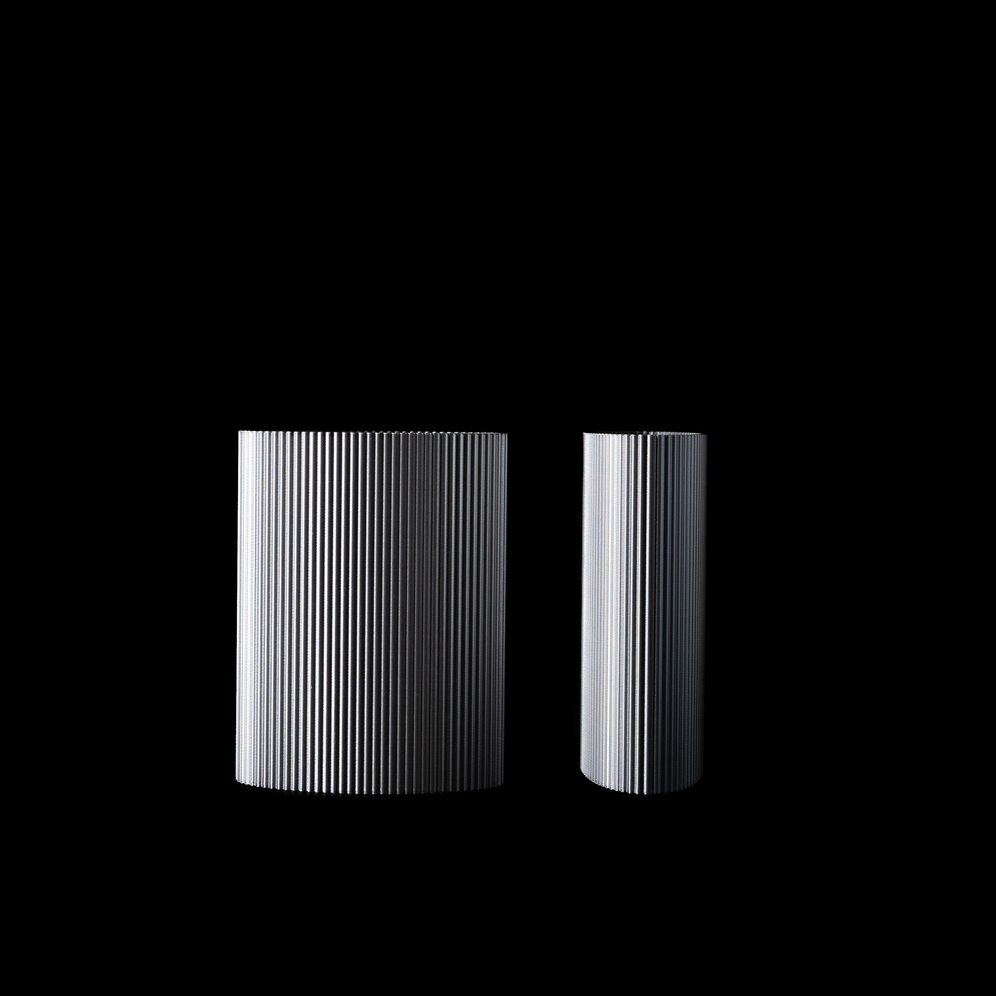 Deux vases Riga en PLA finition Chrome, présentés en vue alternative sur fond noir. La lumière révèle les détails fins des stries verticales.